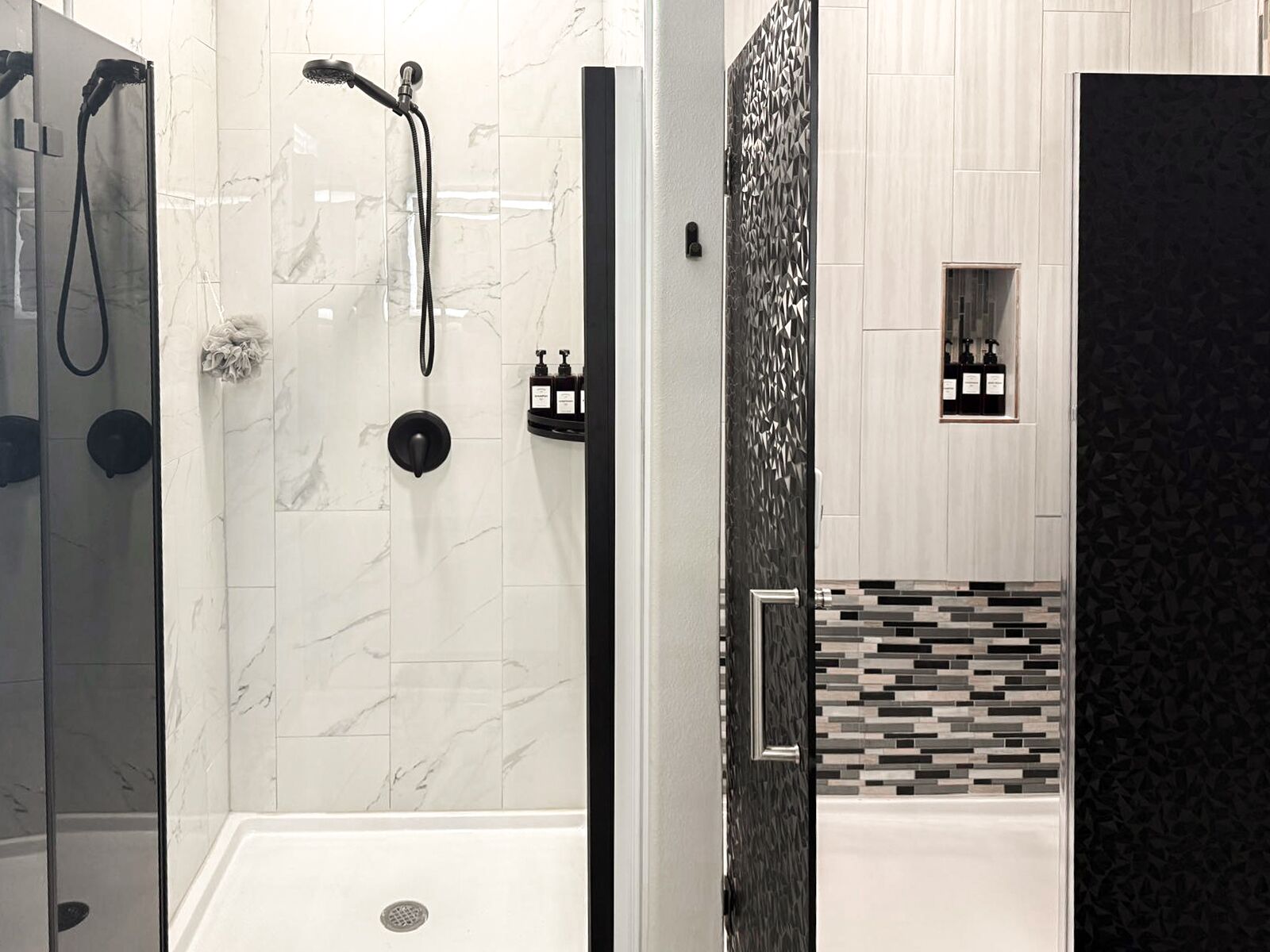 Un baño moderno con ducha envuelta en vidrio, dispensador de toallas negro y tocador con salpicadero de azulejos blanco y negro.