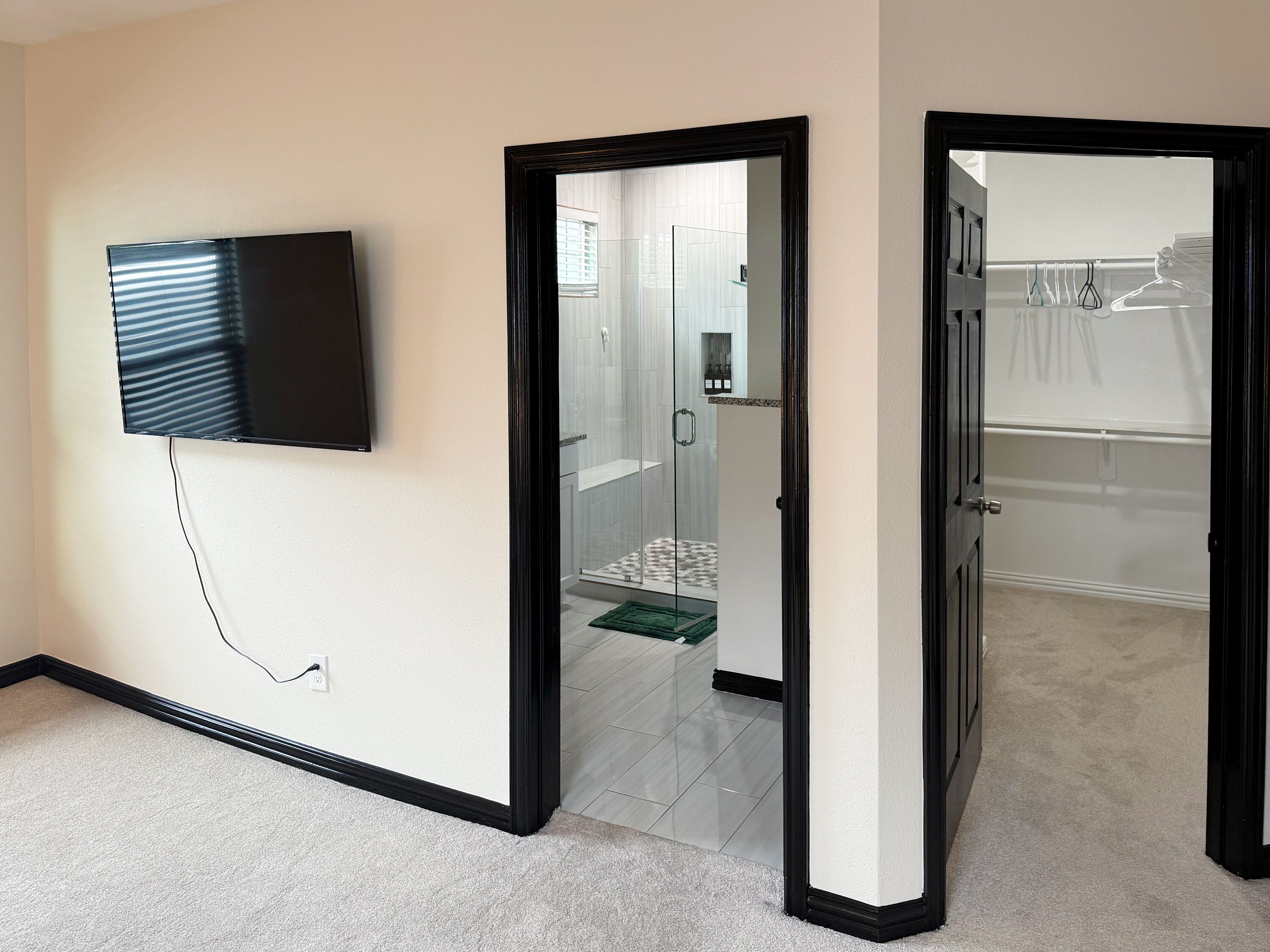 Un pasillo con un televisor de pantalla plana montado en la pared, que conduce a un baño con ducha y retrete.