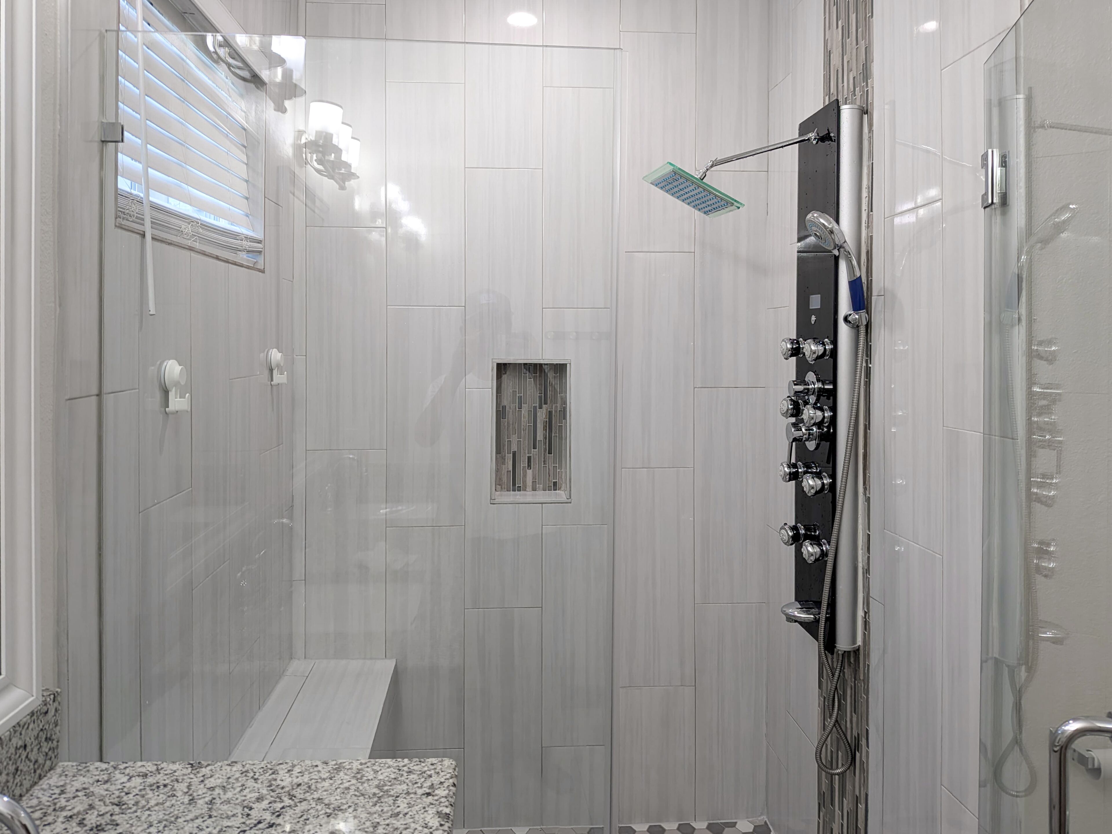 A modern shower with a handheld showerhead, a glass-enclosed shower area, and a tiled floor.