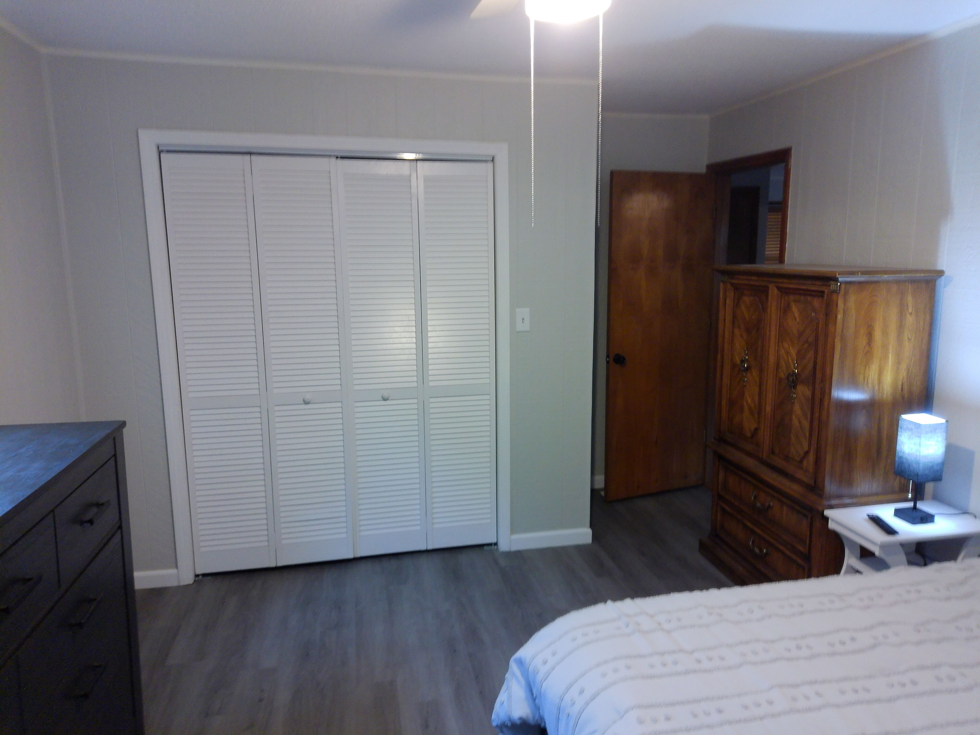 Ein Schlafzimmer mit Bett, Kommode, Kleiderschrank und Schreibtisch mit Lampe.