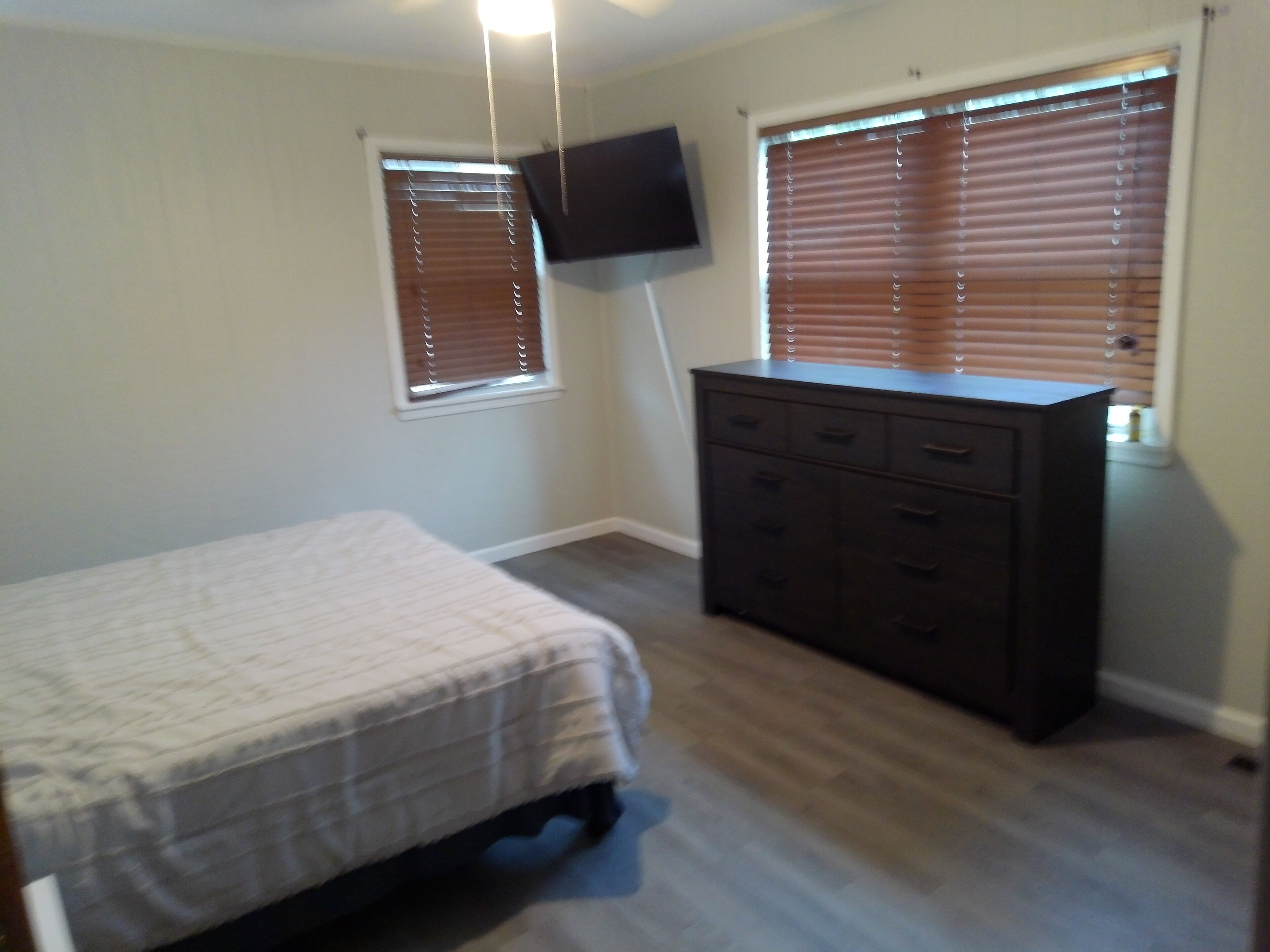 A bedroom with a bed, dresser, and two windows with blinds.
