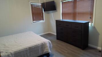 A bedroom with a bed, dresser, and two windows with blinds.