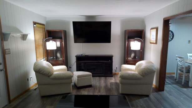 A living room with a flat-screen TV, two armchairs, a coffee table, and a fireplace.