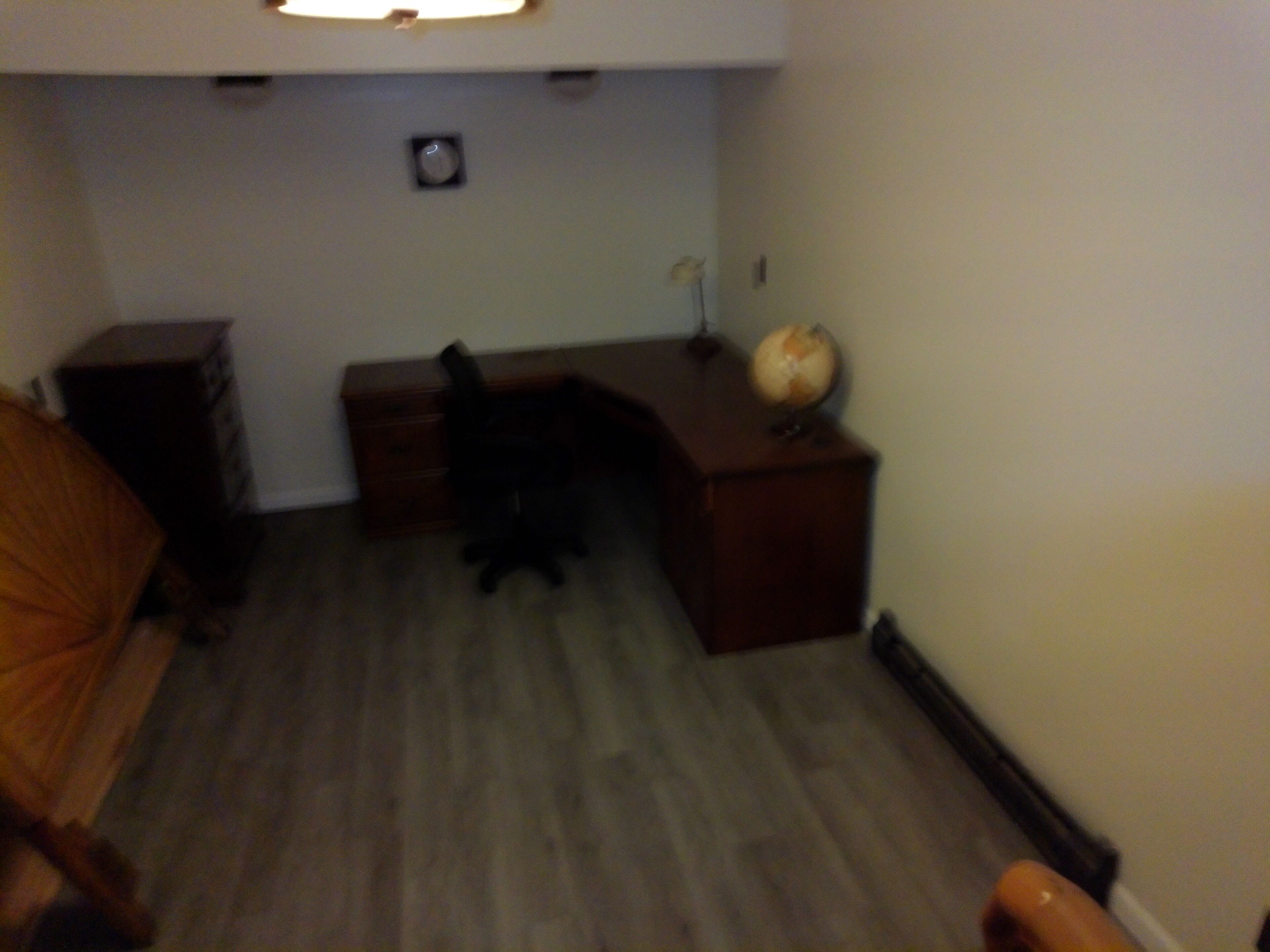Een kleine, zwak verlichte kamer met een bed, een bureau en een wereldbol op een tafeltje.