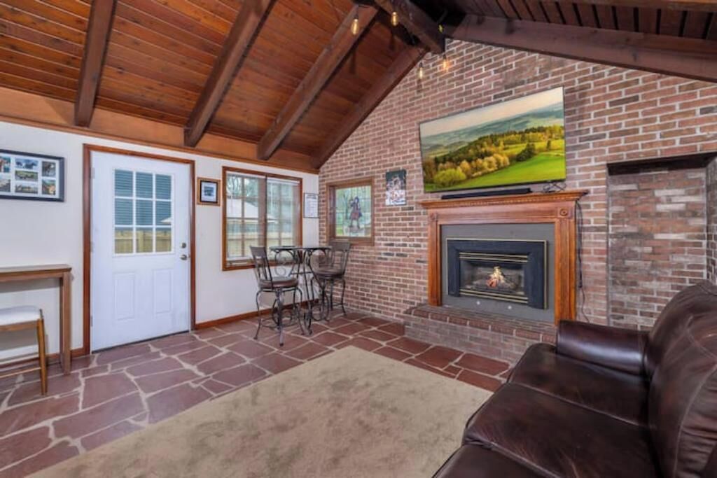 A cozy living room with a fireplace, stone flooring, and a wooden ceiling.
