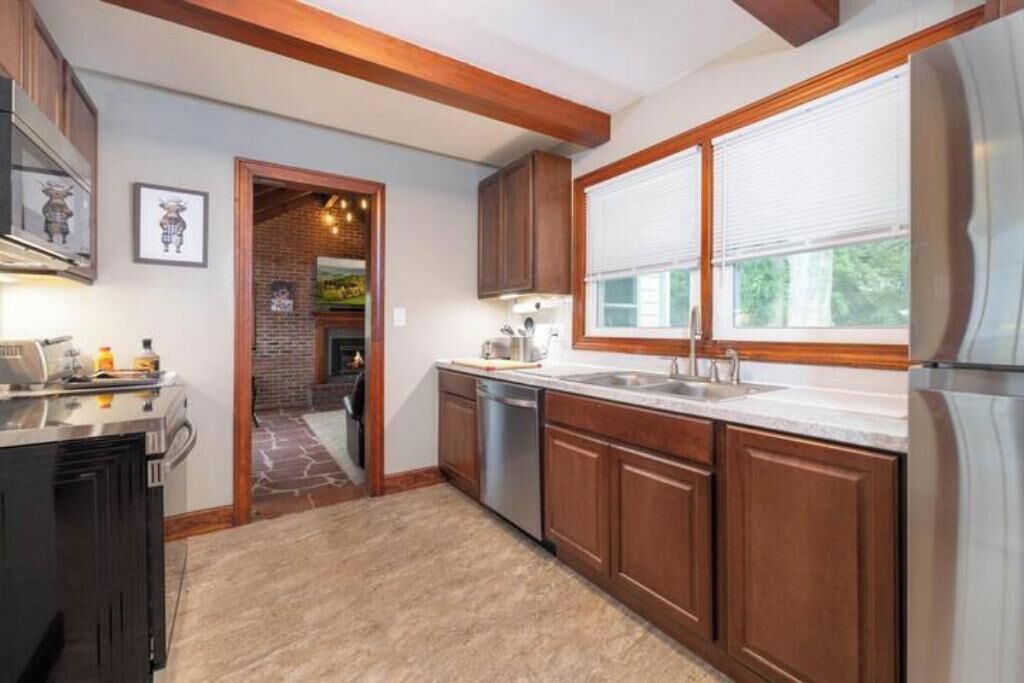 A kitchen with wooden cabinets, a stainless steel refrigerator, and a window with blinds.