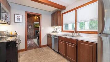 A kitchen with wooden cabinets, a stainless steel refrigerator, and a window with blinds.