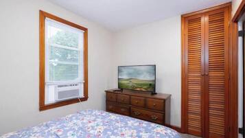 Un dormitorio con cama, cómoda, televisor, ventana con persianas y armario de madera.
