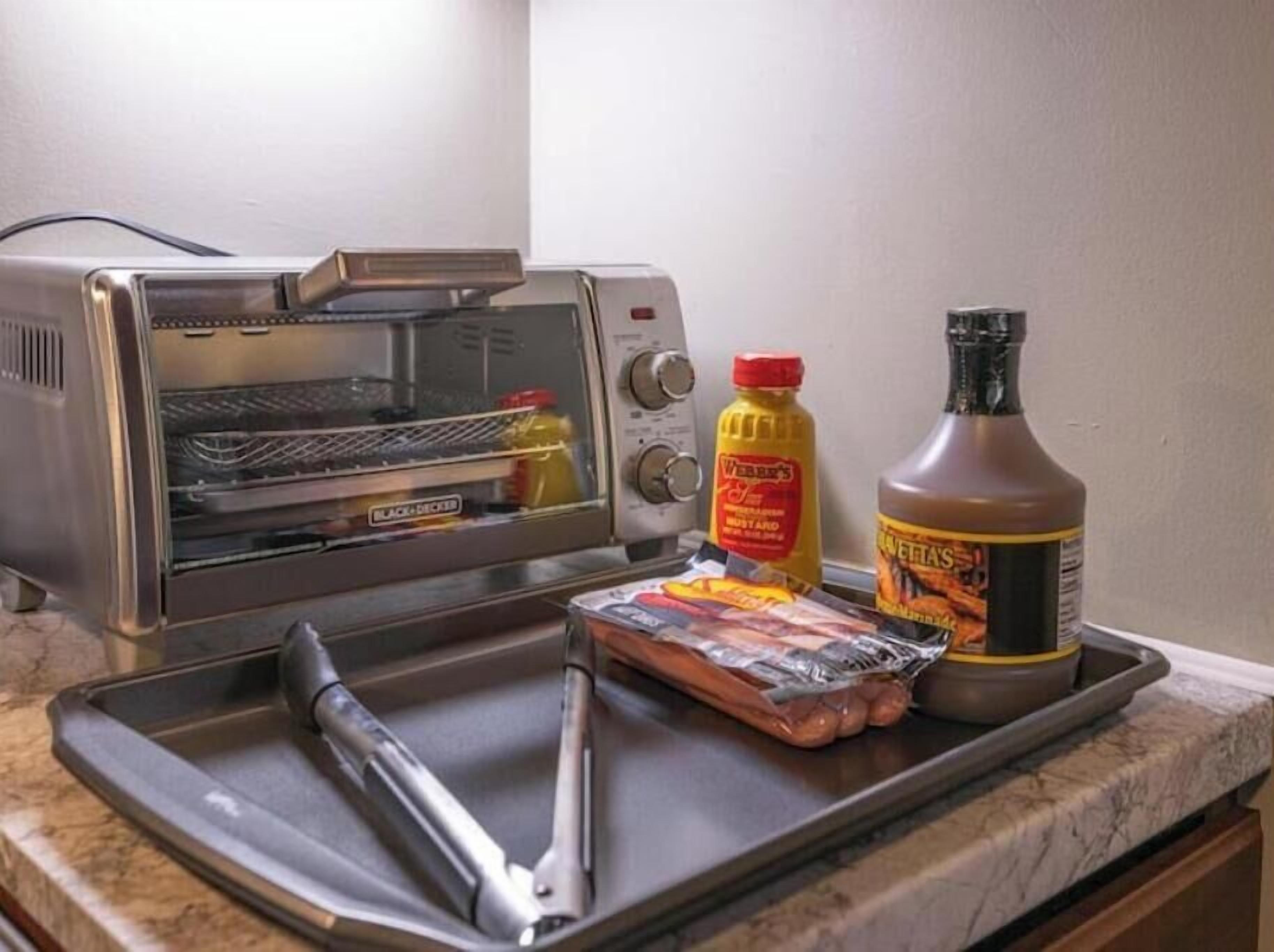 Eine Küche mit einem Toaster, einer Schale mit Fleisch, einer Senfflasche und einer Barbecue-Soße-Flasche.