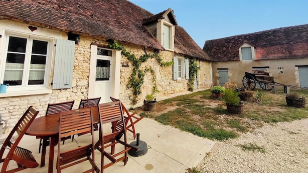 A stone house with a tiled roof, a wooden table and chairs in the yard, and a cart. - Gîte chez Renée (Azay-le-Ferron)