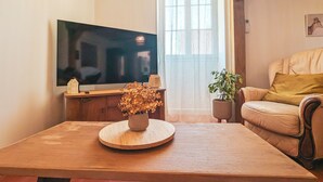 A living room with a flat-screen TV, a wooden coffee table with a vase of dried flowers, a sofa, and a potted plant. - Gîte chez Renée (Azay-le-Ferron)