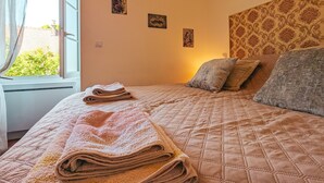 A neatly made bed with a quilted pattern, a window with curtains, and a wall with three small framed pictures. - Gîte chez Renée (Azay-le-Ferron)