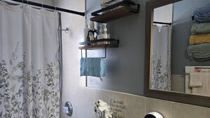 A bathroom with a toilet, sink, and shower curtain. There is a shelf with toiletries and a mirror above the sink.