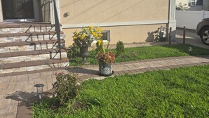 A two-story house with a front porch, a mailbox, and a small garden with potted plants.