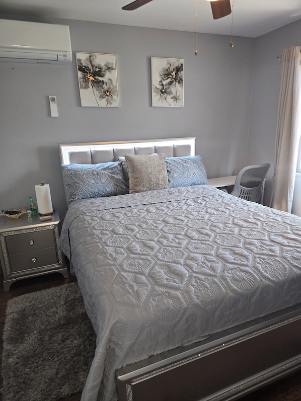 A bedroom with a bed, bedside tables, a chair, artwork on the wall, and a ceiling fan.