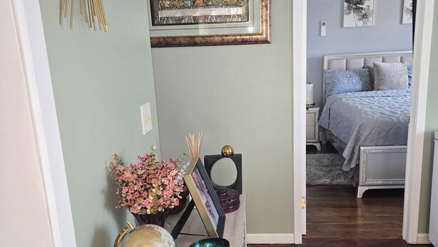 A hallway with a wooden floor leading to a bedroom with a bed and a nightstand.