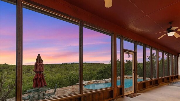 Eine überdachte Terrasse mit großen Fenstern, die einen Pool und eine natürliche Landschaft überblicken.