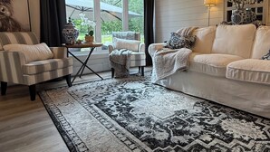 Un salon doté d’une grande fenêtre, d’un lustre et d’un tapis à motifs.