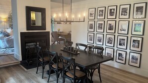 Un coin repas avec une table en bois foncé, six chaises, une cheminée et un mur décoré de photographies en noir et blanc encadrées.
