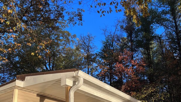 A single-story mobile home with a porch, a small deck, and a window with a view of the surrounding trees.