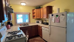 A compact kitchen with a gas stove, microwave, refrigerator, and wooden cabinets.
