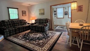A living room with a large sectional sofa, a dining table with chairs, a patterned rug, and a ceiling fan.