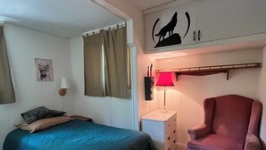 A bedroom with a bed, a chair, a nightstand, a lamp, a wall decoration, and a window with curtains.