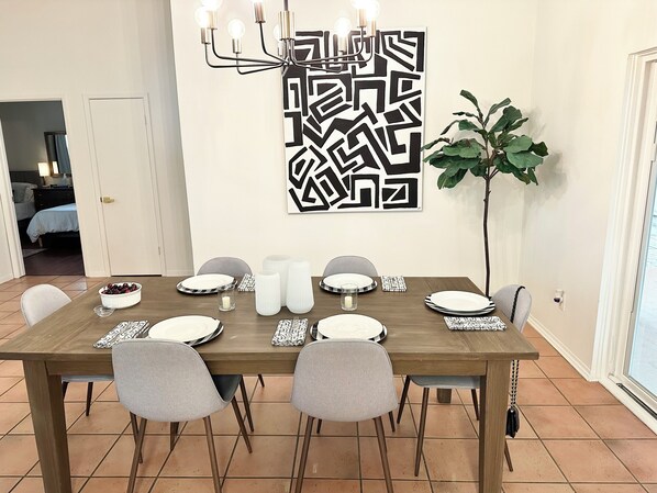 Un comedor con mesa de madera dispuesta para cuatro, sillas grises y una obra de arte moderna sobre la mesa.