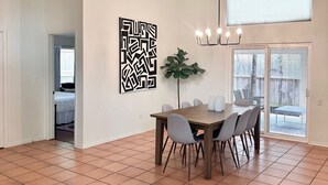 A spacious dining area with a wooden table and chairs, a potted plant, and a modern wall art piece.