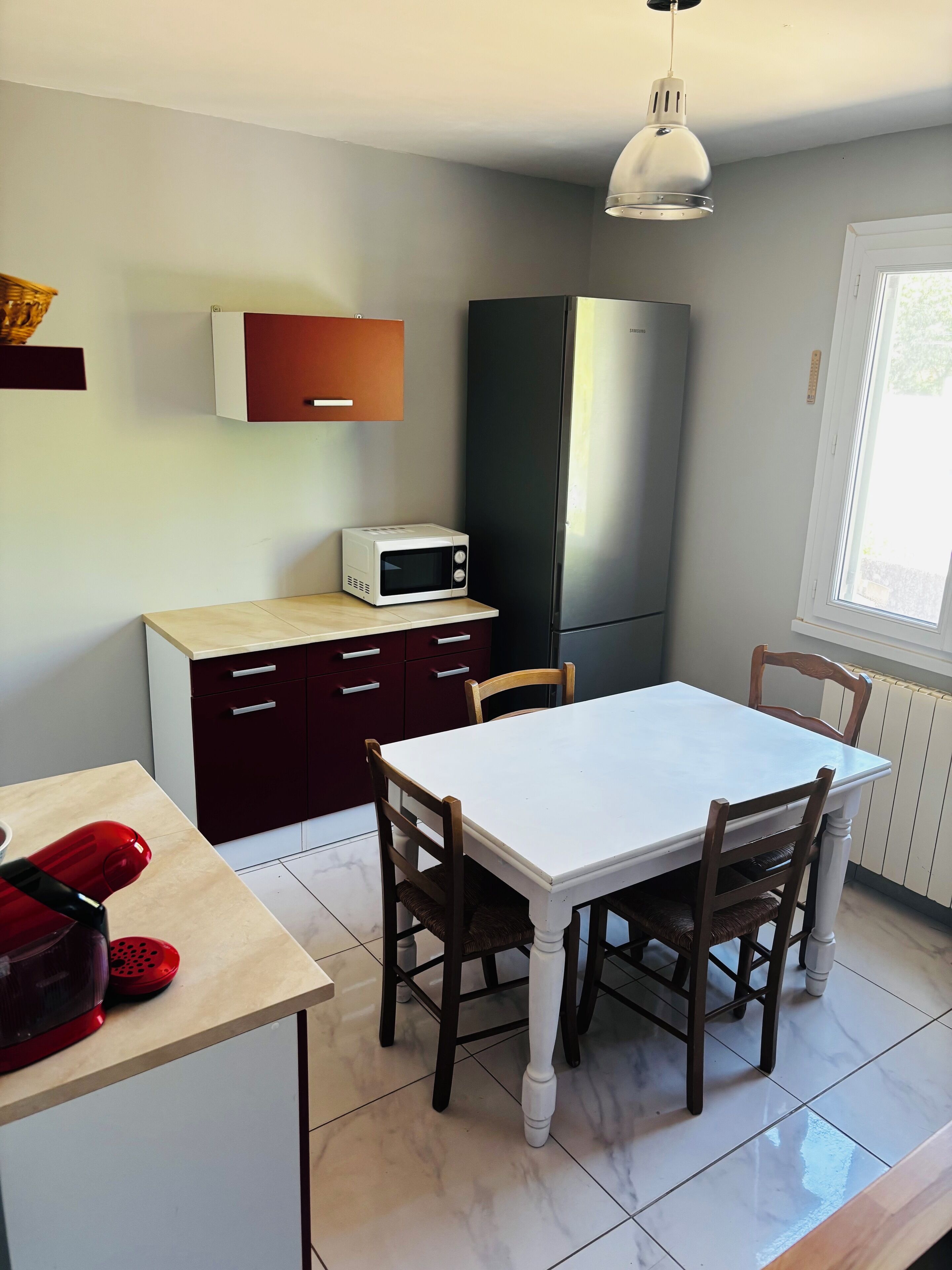 Una cocina compacta con una mesa blanca, sillas de madera, microondas y refrigerador.