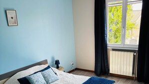 A bedroom with a bed, a nightstand, a lamp, a window with curtains, and a radiator. - 6-person house with garden in quiet neighborhood (Cournonterral)