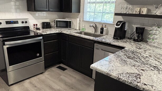 A modern kitchen with dark cabinetry, a stainless steel stove, a microwave, and a coffee maker. - Green Cottage / Explore Trails, Ride Bikes & Golf! (Bella Vista)