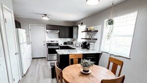 A modern kitchen with white cabinets, a central island, and a dining area with a round table and chairs. - Green Cottage / Explore Trails, Ride Bikes & Golf! (Bella Vista)