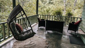 A porch with wicker chairs and a woven rug, overlooking a forested area. - Green Cottage / Explore Trails, Ride Bikes & Golf! (Bella Vista)