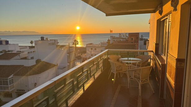 A balcony with a view of the sunset over the sea, wicker furniture, and a tiled floor. - Carihuela Cristal - Beach + Swimming Pool + Terrace + Sea View (Torremolinos)