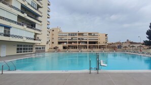 A swimming pool surrounded by multi-story buildings with balconies, a lifeguard chair, and umbrellas. - Carihuela Cristal - Beach + Swimming Pool + Terrace + Sea View (Torremolinos)