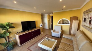 A living room with a TV, a white armchair, a beige sofa, a glass coffee table, and a red cabinet. - Carihuela Cristal - Beach + Swimming Pool + Terrace + Sea View (Torremolinos)