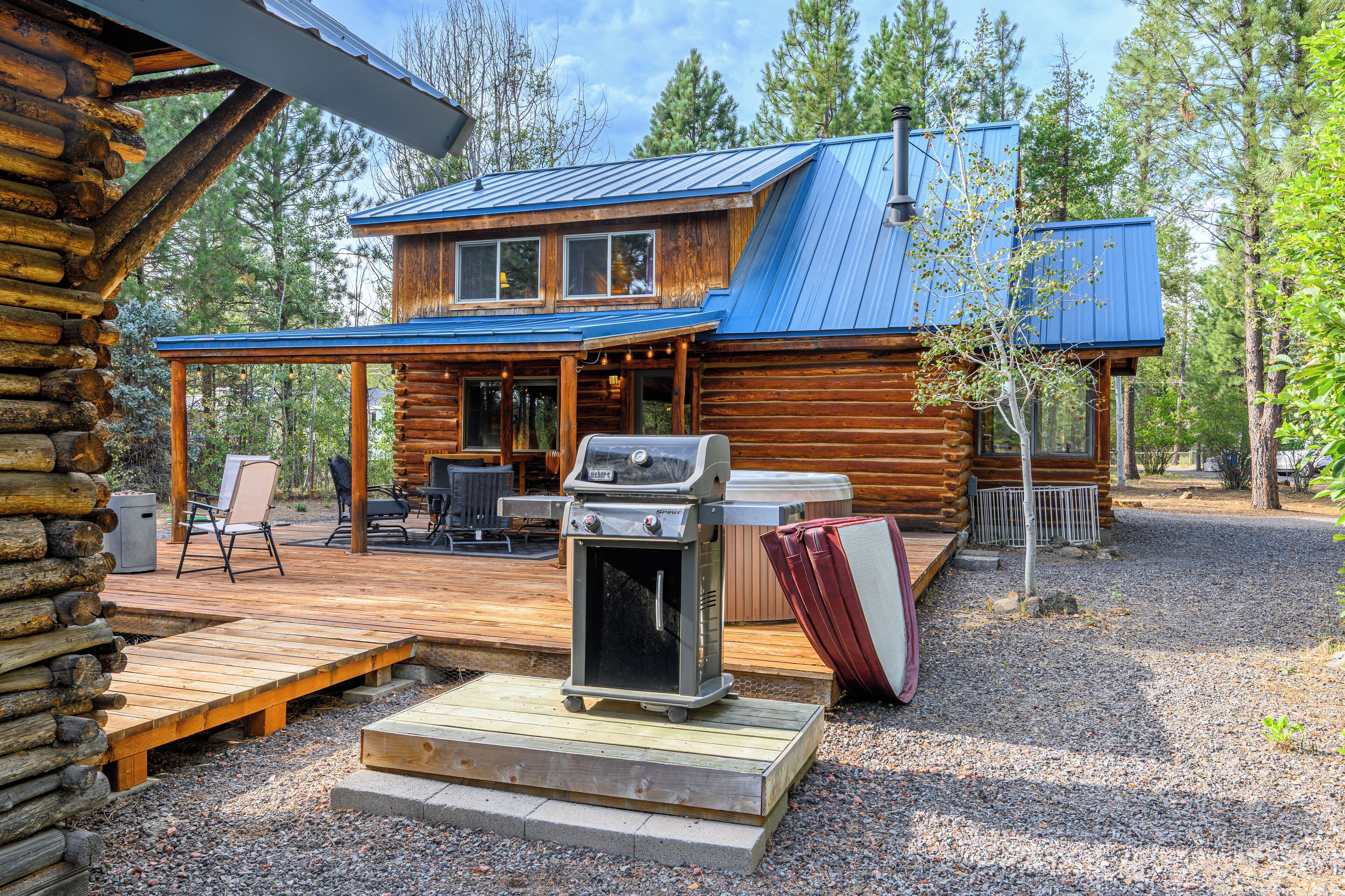 A log cabin with a deck, outdoor seating, and a grill.