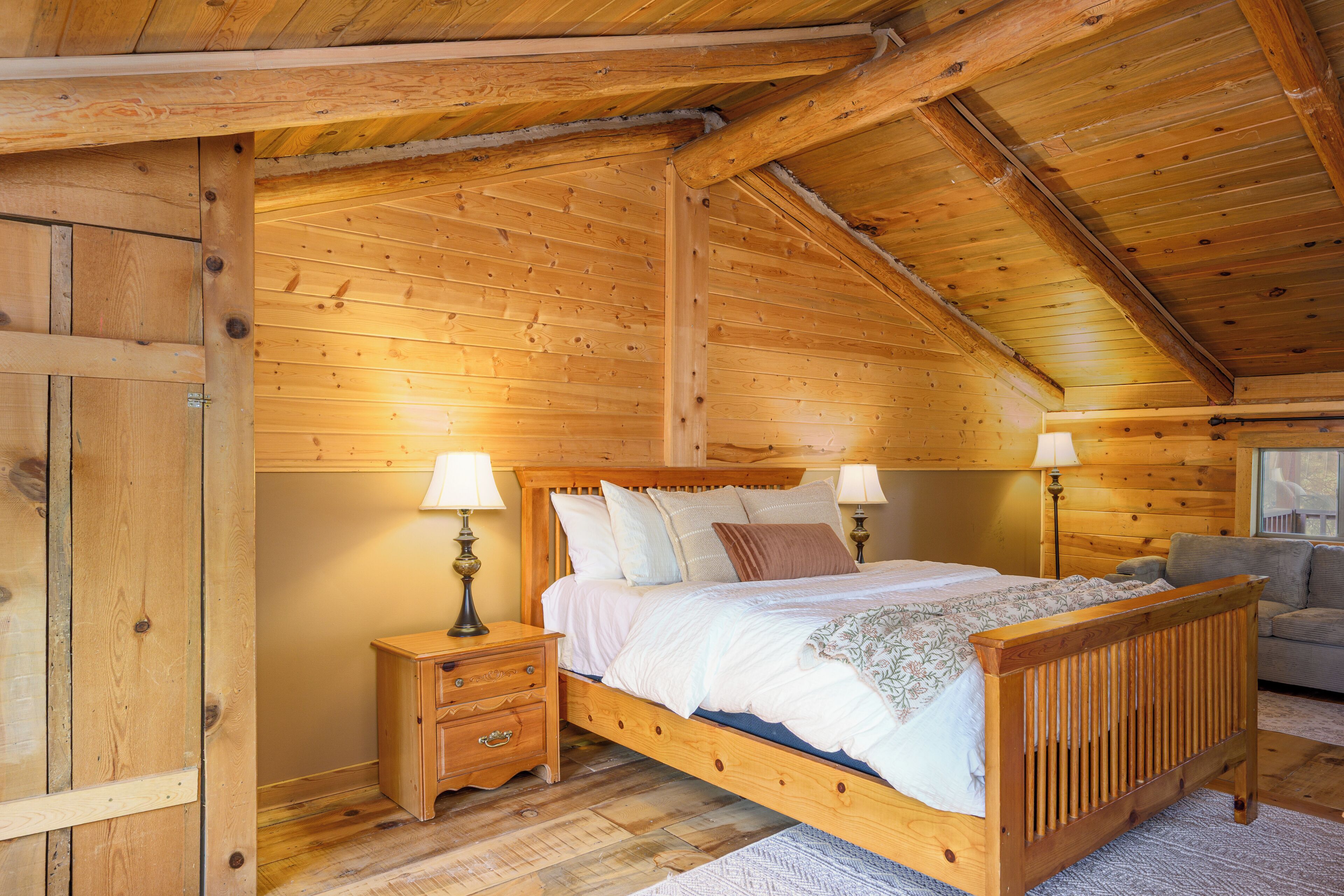 A wooden bedroom with a bed, nightstands, and a sofa.