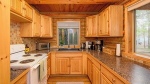 Une cuisine avec des meubles de rangement en bois, une cuisinière, un four à micro-ondes et une fenêtre donnant sur les arbres.