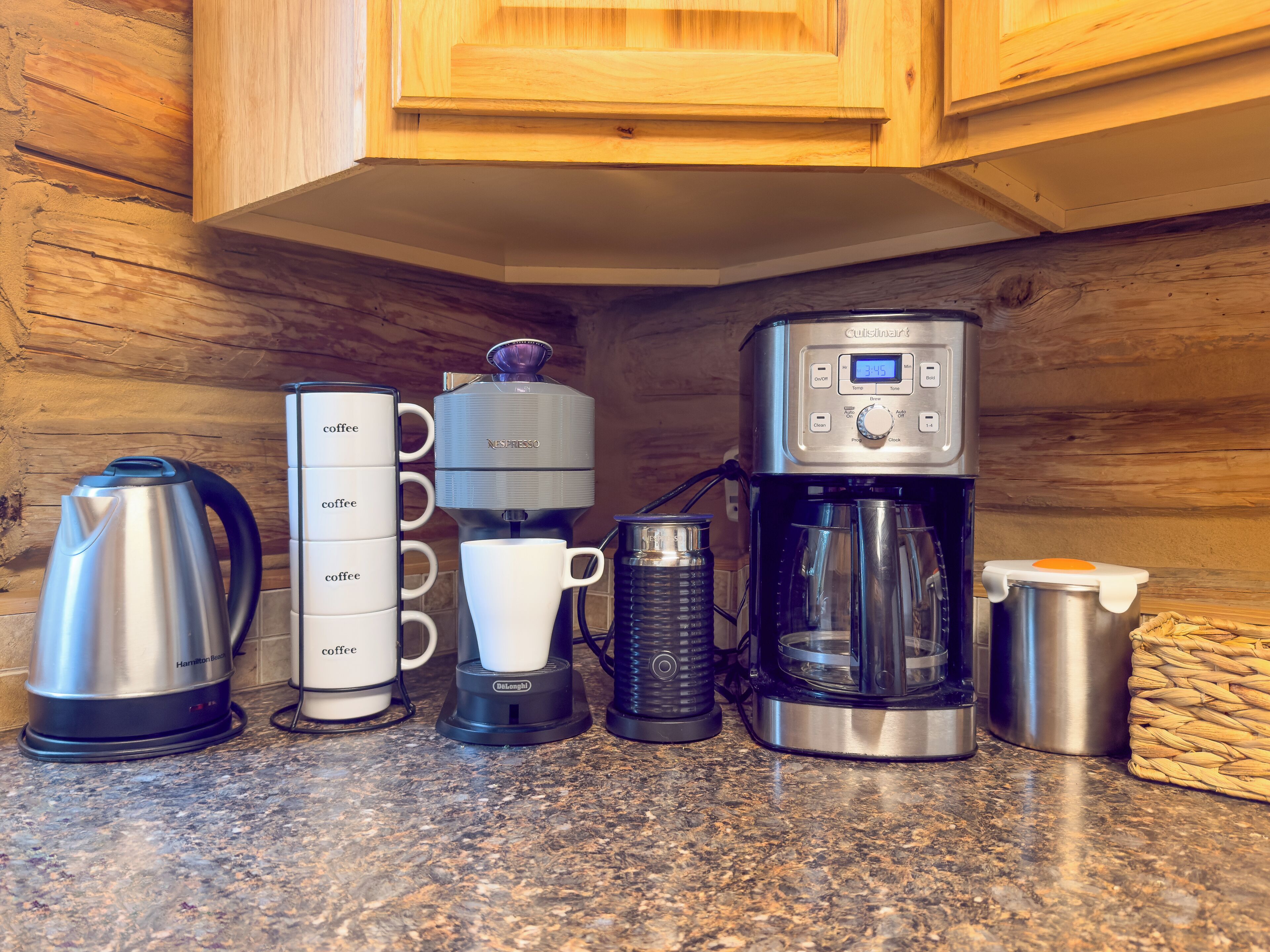 A kitchen counter with a coffee maker, a kettle, a coffee grinder, a coffee pot, and a mug.