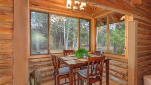 Une cabane en bois avec une table et des chaises, de grandes fenêtres et une vue sur la forêt.