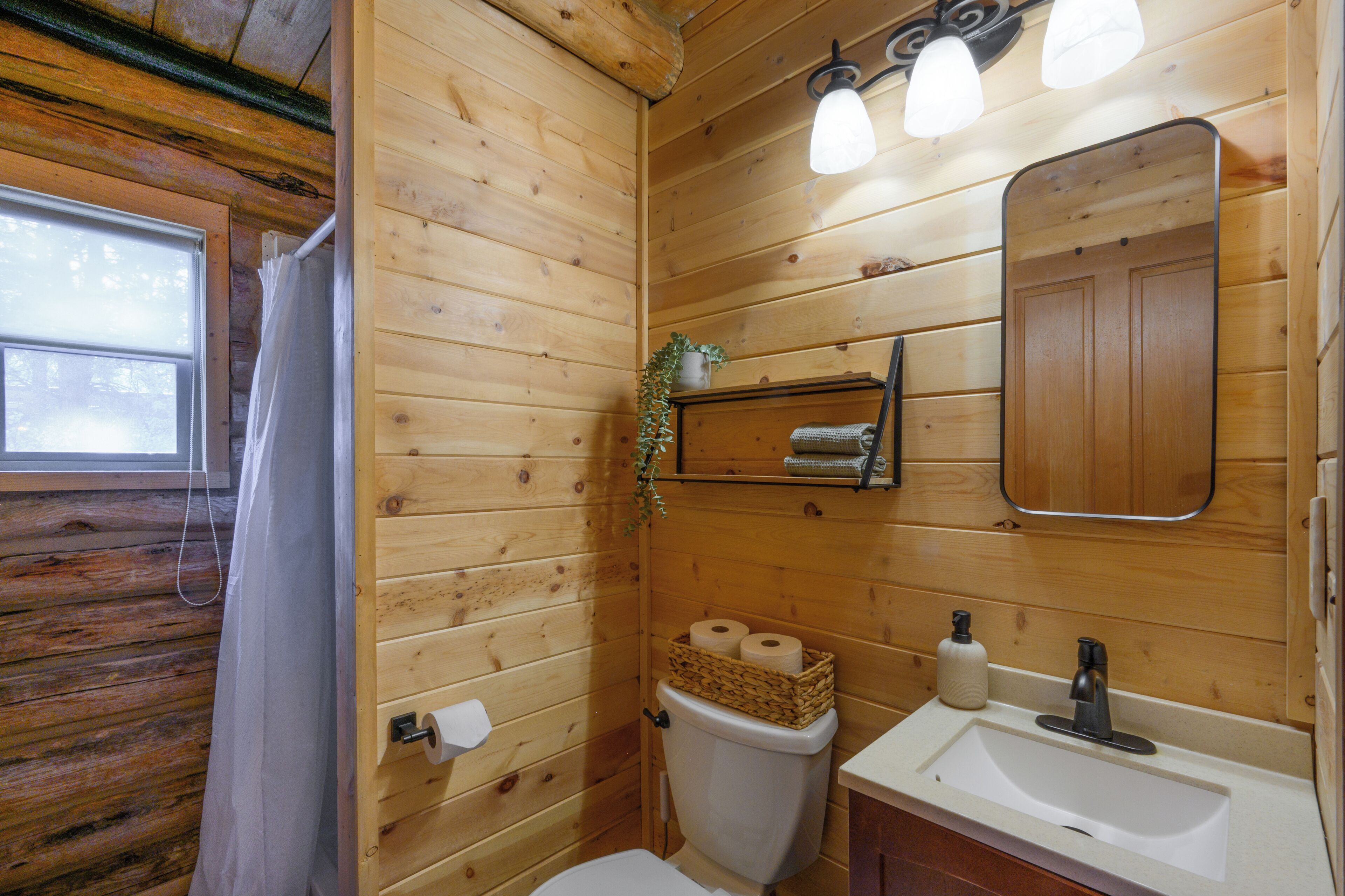 Ein Badezimmer einer Holzhütte mit Toilette, Waschbecken und Spiegel.