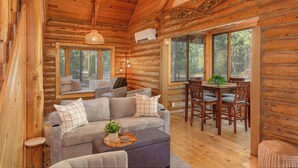 L’intérieur d’une cabane en rondins, avec un canapé, une table à manger, des chaises et un luminaire suspendu.