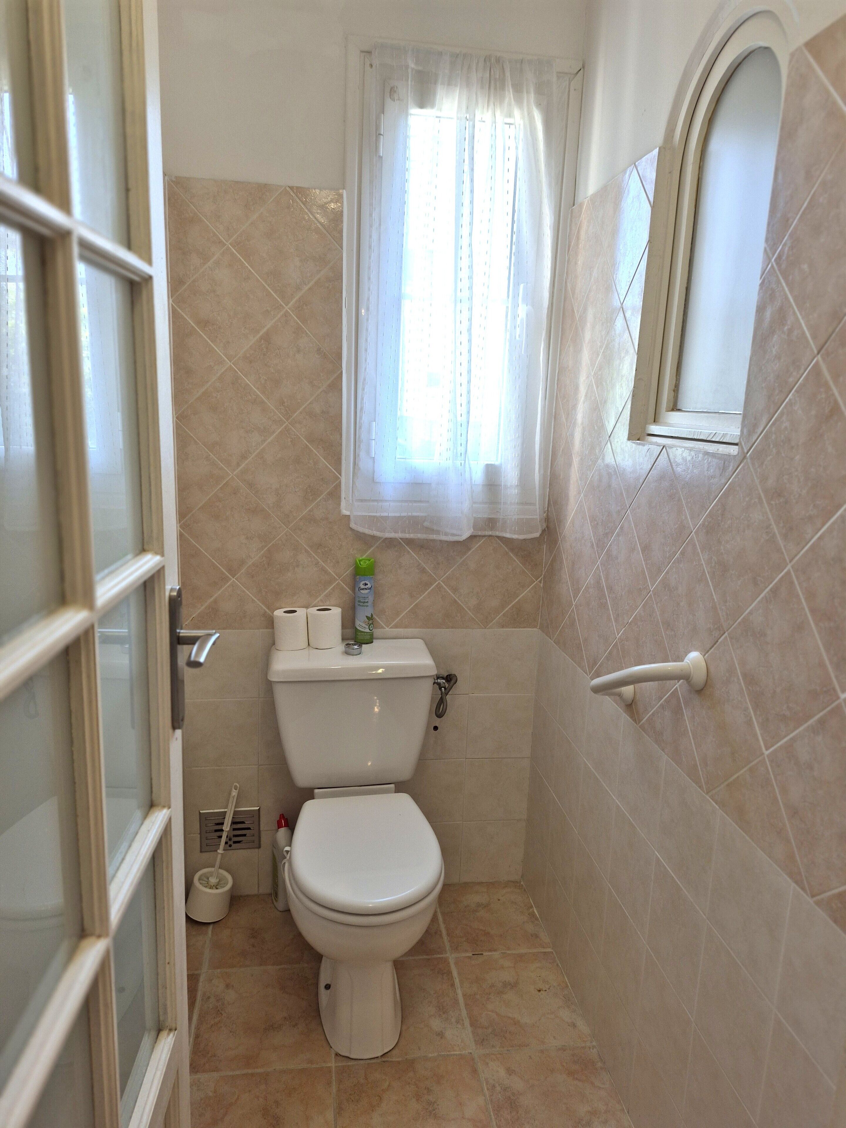 A bathroom with a toilet, a window with a curtain, and a shower area.