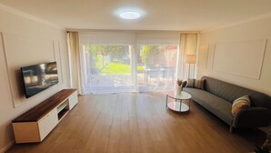 Un salon moderne doté d’un téléviseur à écran plat, d’un canapé, d’une table basse et d’une porte-fenêtre coulissante donnant sur une terrasse extérieure.