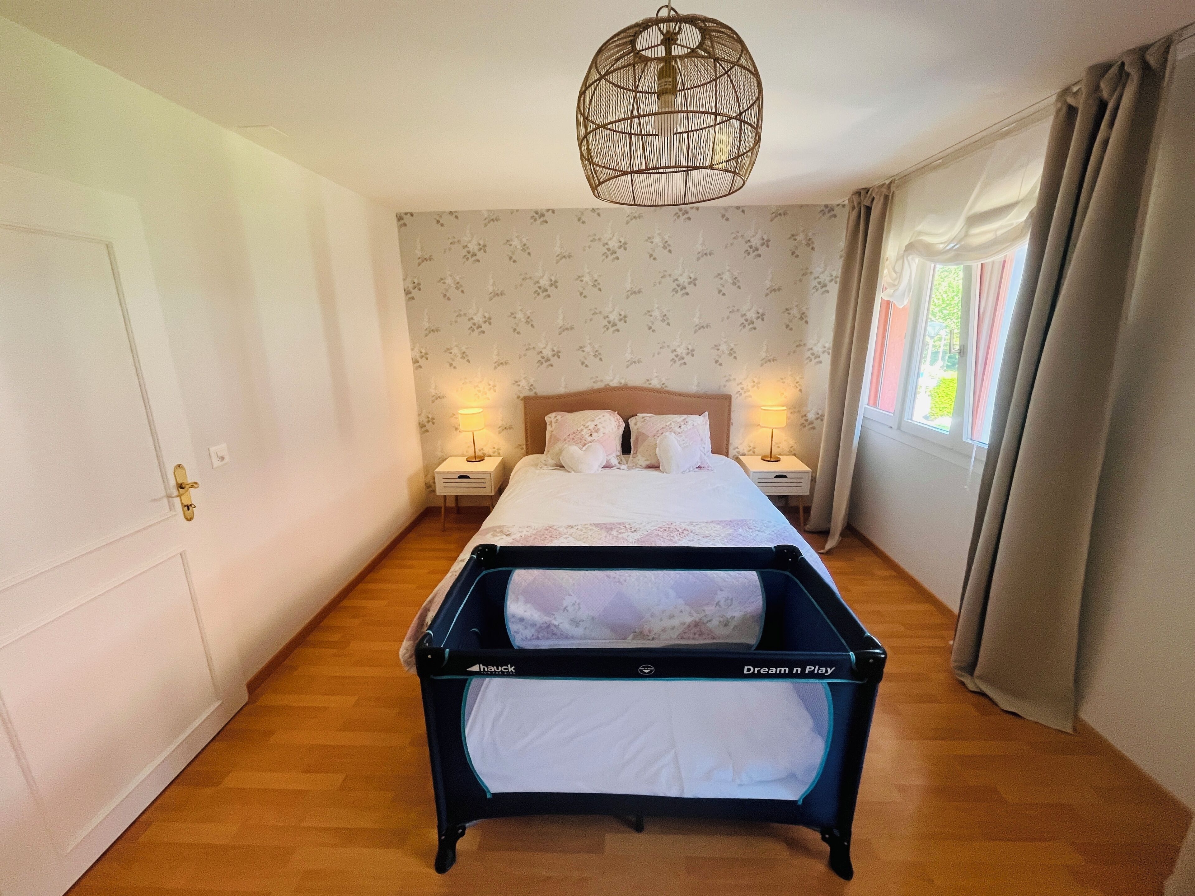 Un dormitorio con cama, lámparas de noche, una lámpara colgante y una ventana con cortinas.