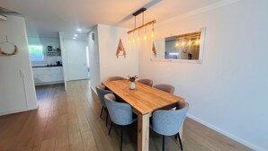 Un espace repas moderne avec une table en bois et des chaises grises, un luminaire suspendu et un miroir au mur.