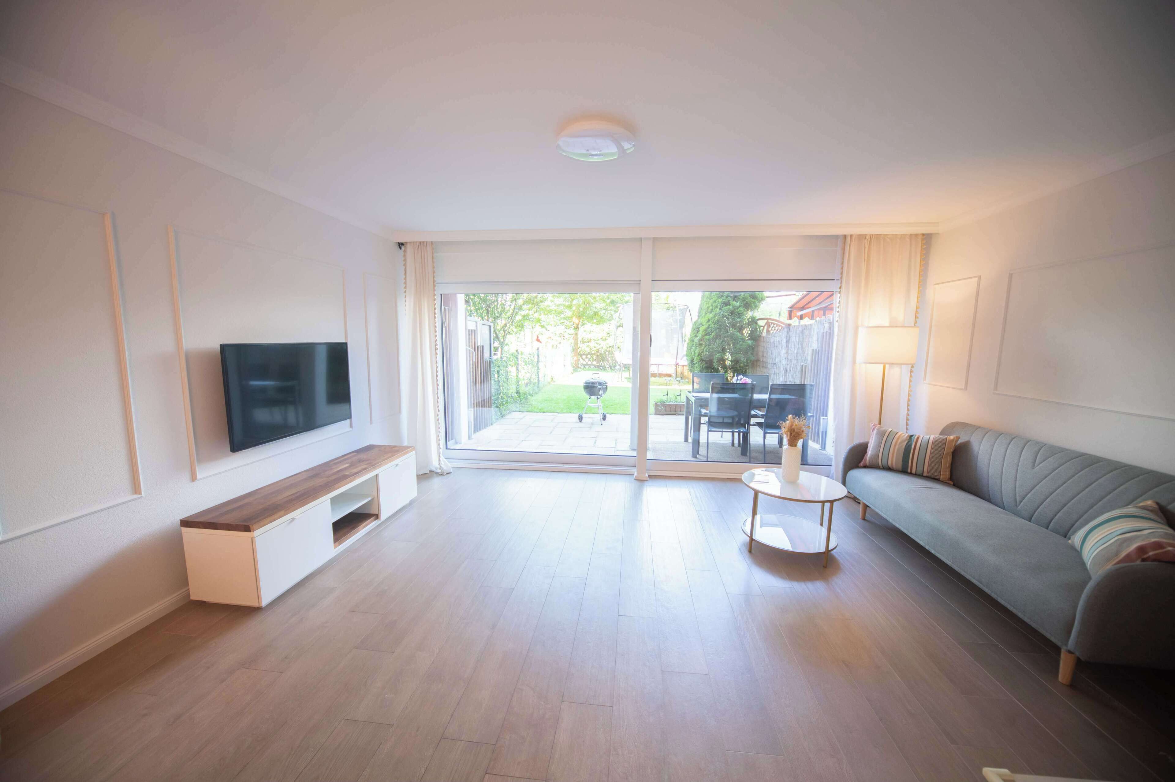 Una sala de estar moderna con una televisión de pantalla plana, un sofá, una mesa de centro y un suelo de vidrio corredera que da a un área exterior.