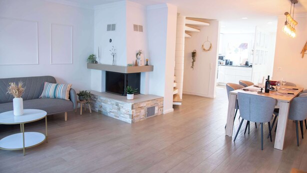 Un salon moderne avec une cheminée, un coin repas avec une table et des chaises, et une cuisine visible à travers une porte ouverte.